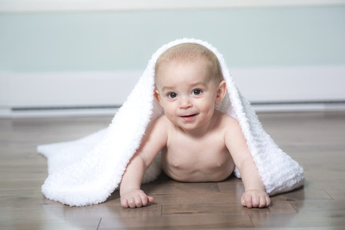 A baby smiling and crawling on a wooden floor with a white towel over it