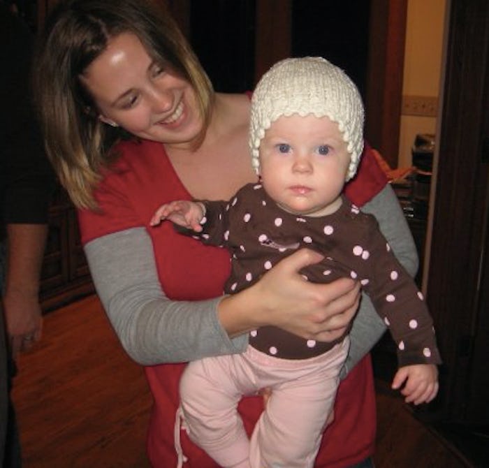 A mom holding her toddler of one year old who is wearing a knitted hat a polkadot shirt and pink pan...
