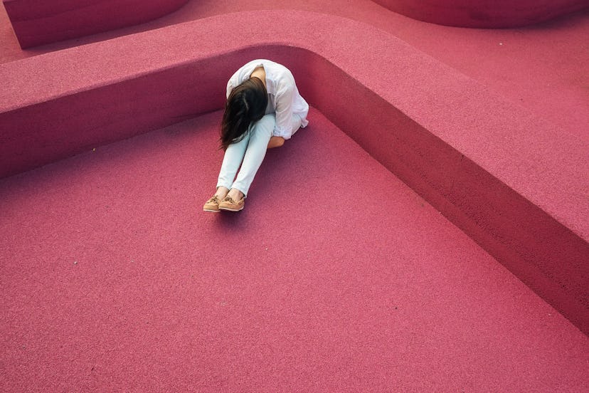 A woman with Endometriosis sitting in a corner of a red room feeling sad and depressed