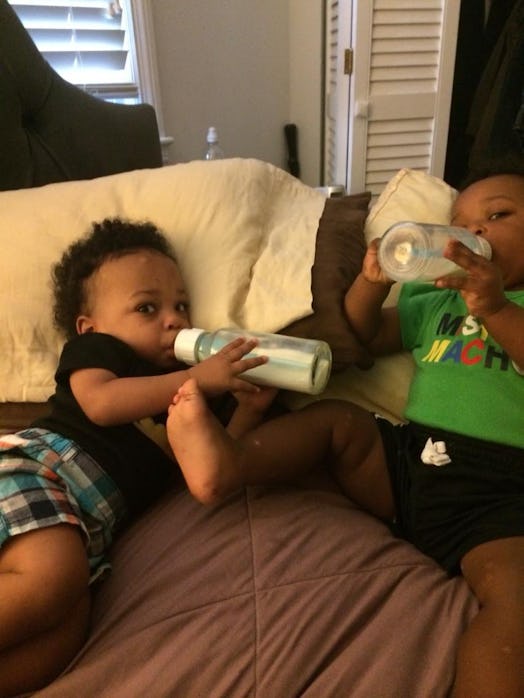 Two baby boys drinking milk from bottles while lying on a bed