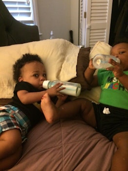 Two baby boys drinking milk from bottles while lying on a bed