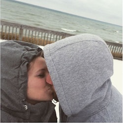 Chaunie Brusie and her husband both wearing grey hoods over their heads while kissing outside in the...