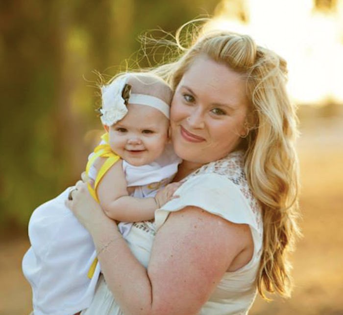 Woman in a white gown holding her baby outside on a sunny day