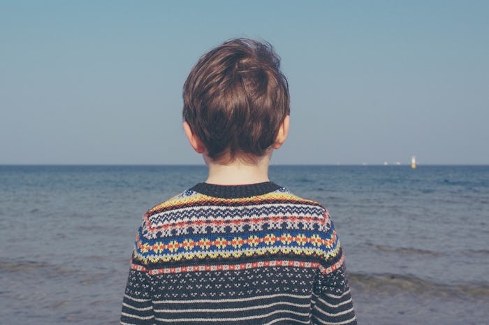 Kid in a multicolored jumper looking out toward the ocean
