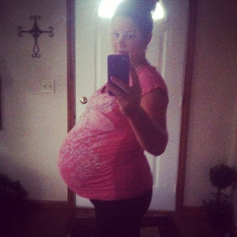 Pregnant woman in pink t-shirt taking a selfie in the mirror