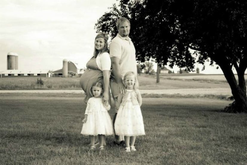 Photograph of a pregnant woman, her husband, and their two daughters on the meadow