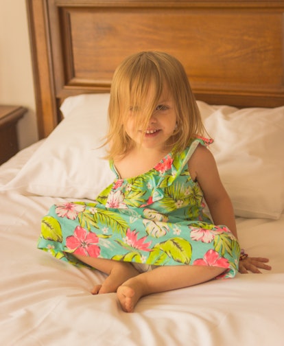 An three year old little girl sitting on the bed in her summer dress