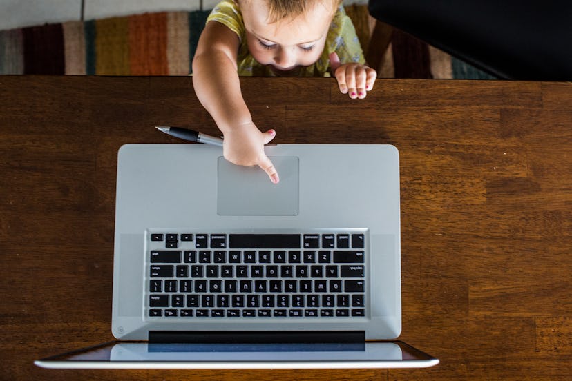 Toddler touching the mousepad of his work from home moms laptop