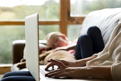 Work from home mom on her laptop while her daughter sleeps beside her on the couch