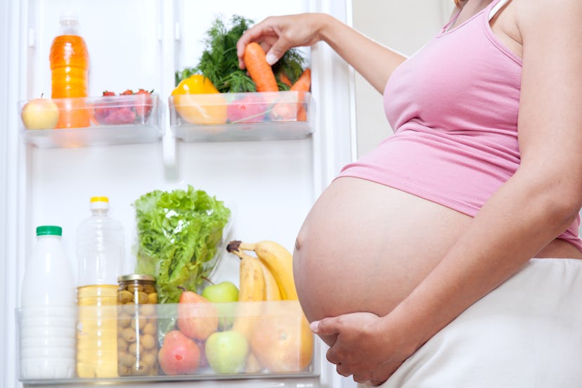A pregnant woman taking veggies to eat from her fridge to protect herself from Preeclampsia 