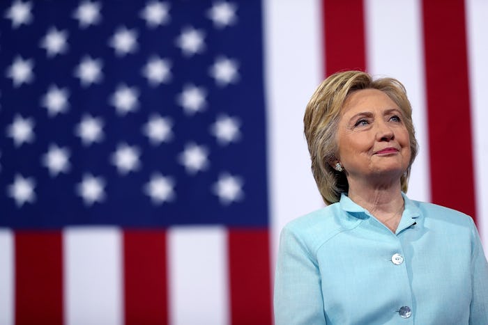 Hillary Clinton posing in a light blue blazer in front of a USA flag