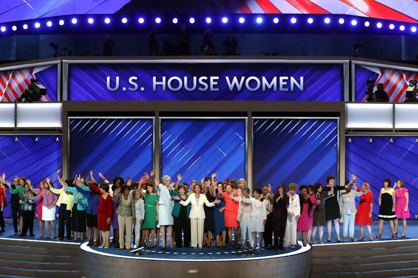A large group of women posing for the picture on the stage underneath the US House Women sign