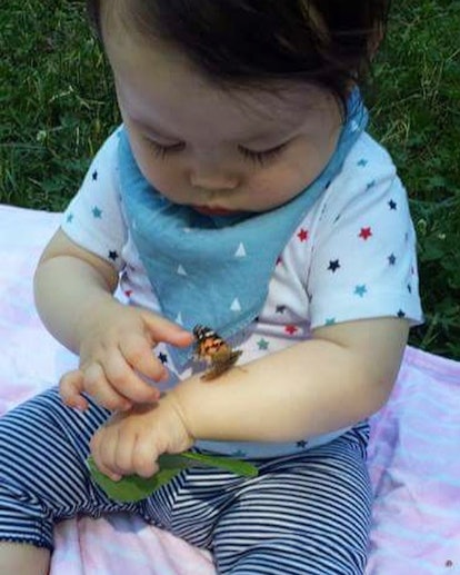 A baby sitting on the grass and a butterfly is on his hand