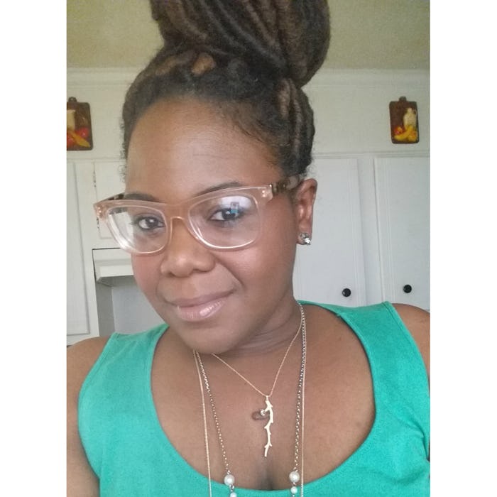 A woman wearing glasses with her hair in a high bun smiling while taking selfie