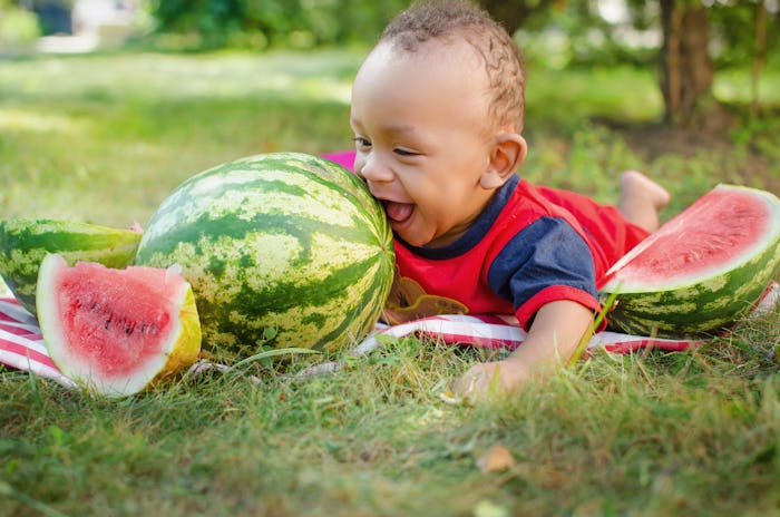A little boy lying next to a watermelon on a picnic blanket