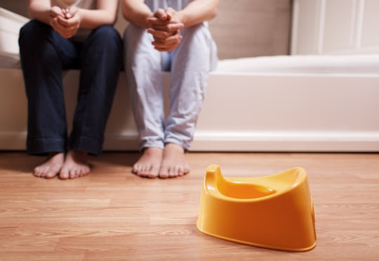 A closeup of the legs of two parents sitting on a bed with a potty in front of them waiting to potty...