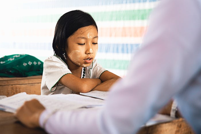 A kid sitting in front of his teacher in the classroom