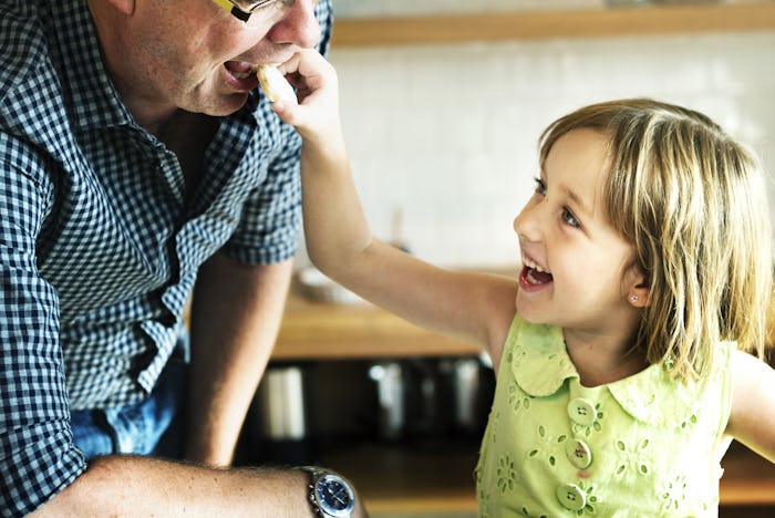 A happy kid smiling and putting a snack in her dads mouth as the dad cares about healthy eating
