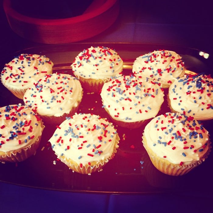 A tray of cupcakes with white frosting and sprinkles made my a pregnant woman who is nesting