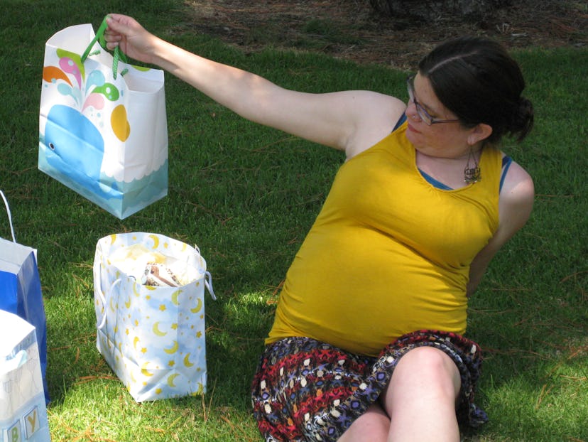 Pregnant Samantha Taylor sitting on the grass, wearing colorful pants and a yellow t-shirt, holds a ...