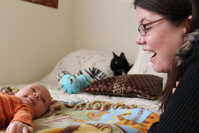 Samantha Taylor sitting next to her baby who is lying on his bed and playing