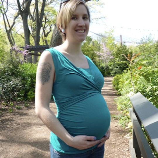 Kimberly Zapata smiling in a teal top with her hands supporting her pregnant stomach