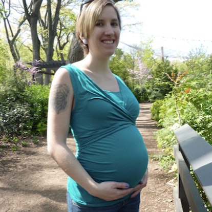 Kimberly Zapata smiling in a teal top while holding her pregnant stomach with her hands