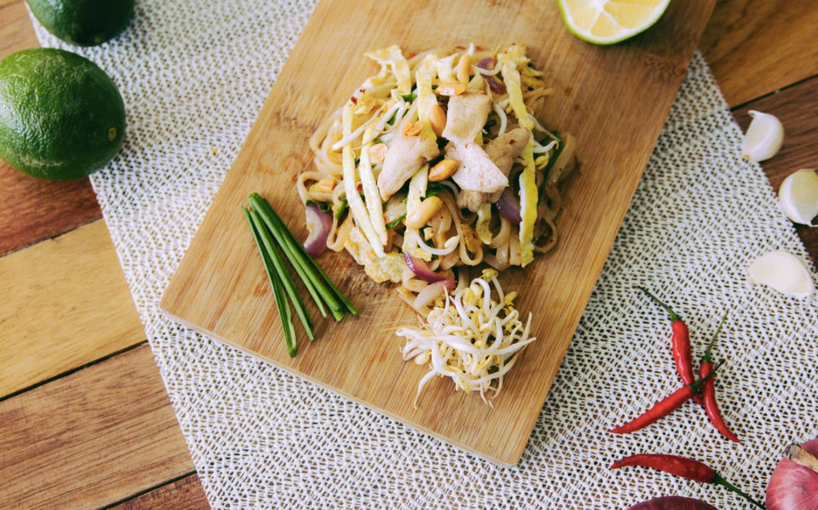 Mushrooms, chives, bean sprouts and a lime on a cutting board, chillis and garlic beside it