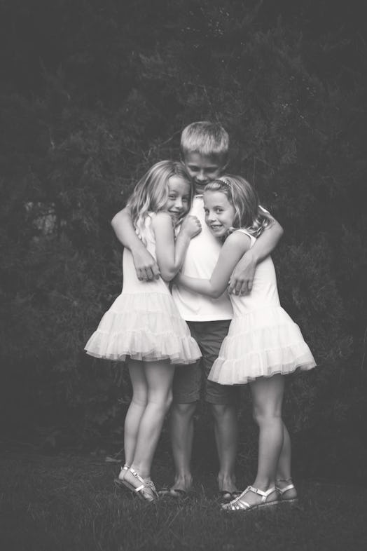 Two girls in ballet tutus hugging a boy in the middle and they're all smiling