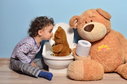 A potty-training boy kissing his stuffed bear on the toilet seat while a large teddy bear is holding...