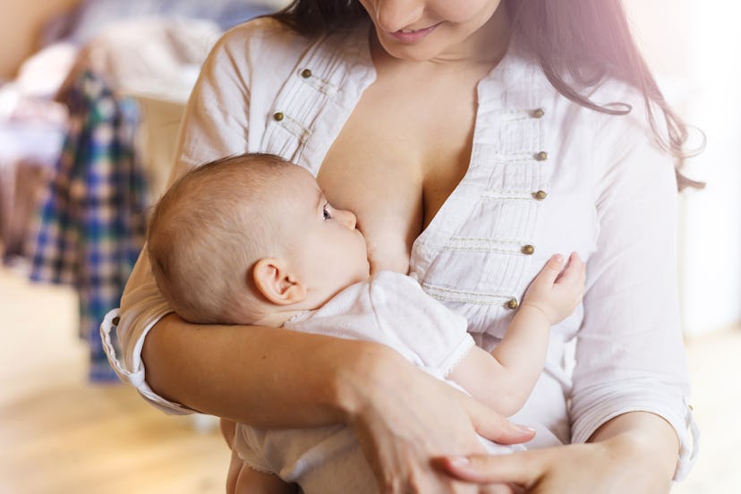 A woman in a white button up shirt breastfeeding her baby in their bedroom