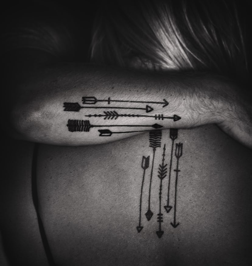 A man's arm hugging a woman's back with the matching arrow-shaped tattoos