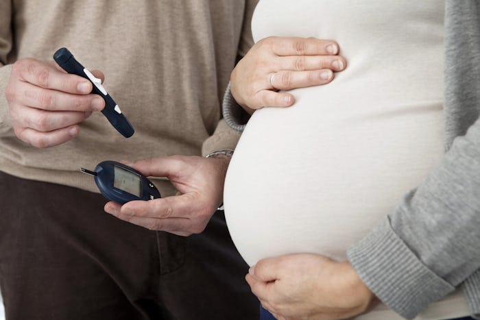 A father holding a pen and Diabetes reading device next to his pregnant wife who has Gestational Dia...