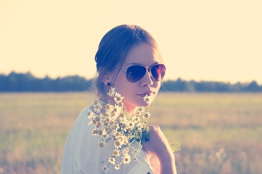 A hippie mom on a field, holding a bouquet of daisies.