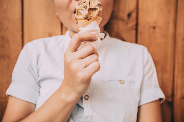 Kid in a dress shirt lying on a wooden floor while eating an ice cream cone