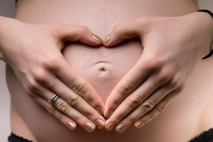 a woman making a heart with her hands over her pregnant belly