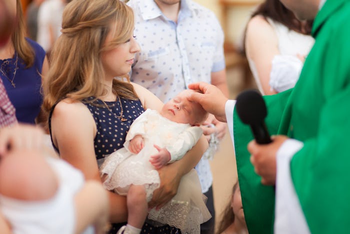 A mom holding her baby as it gets baptized 
