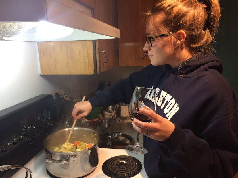 A girl with messy hair and wearing glasses preparing dinner with glass of wine in her hand