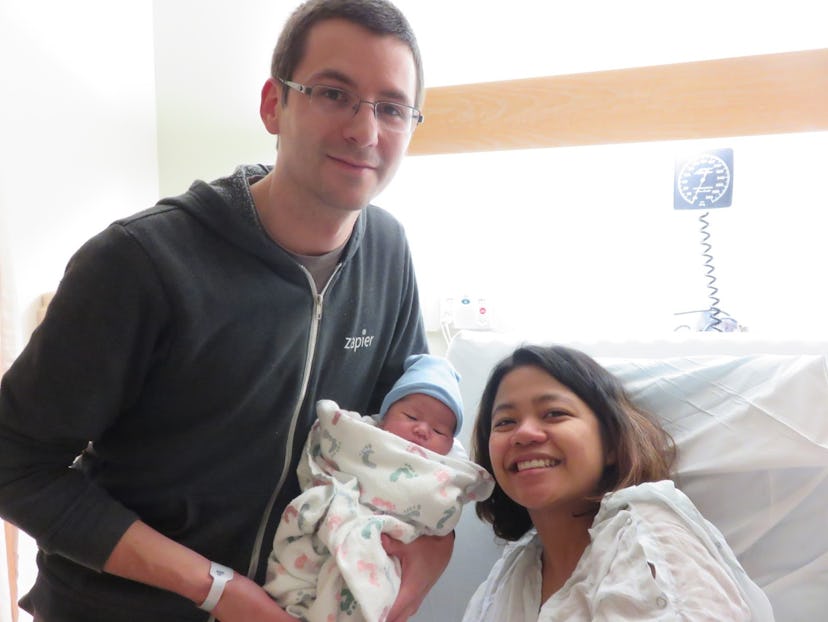 A woman posing for a picture with her husband and their newborn in the hospital