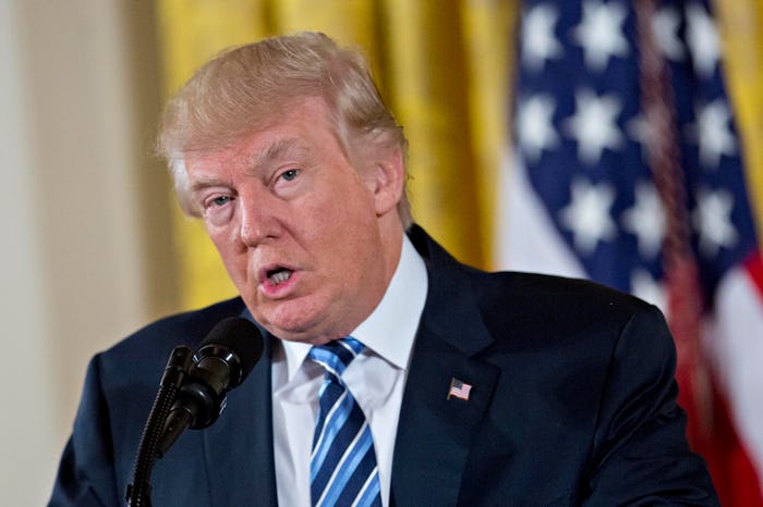 Donald Trump speaking at a press conference wearing a black suit and blue striped tie