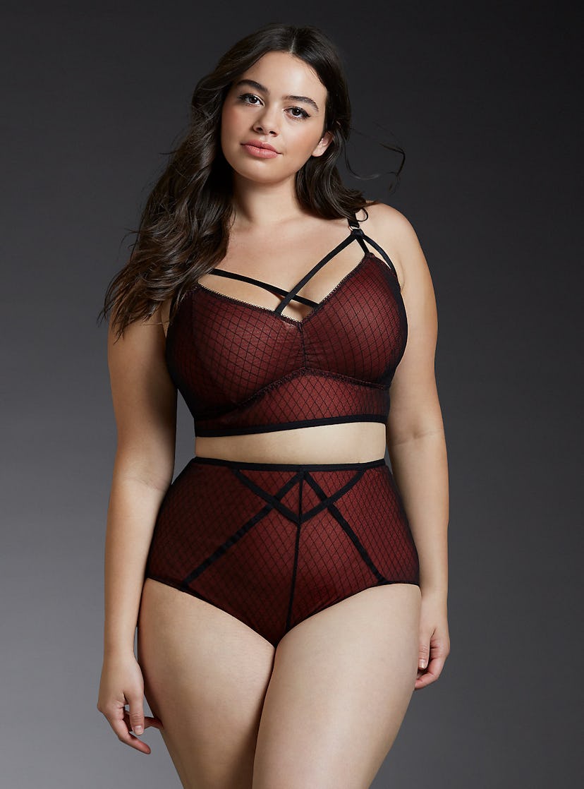 A model posing in strappy high waisted panties and in a matching strappy mesh bralette