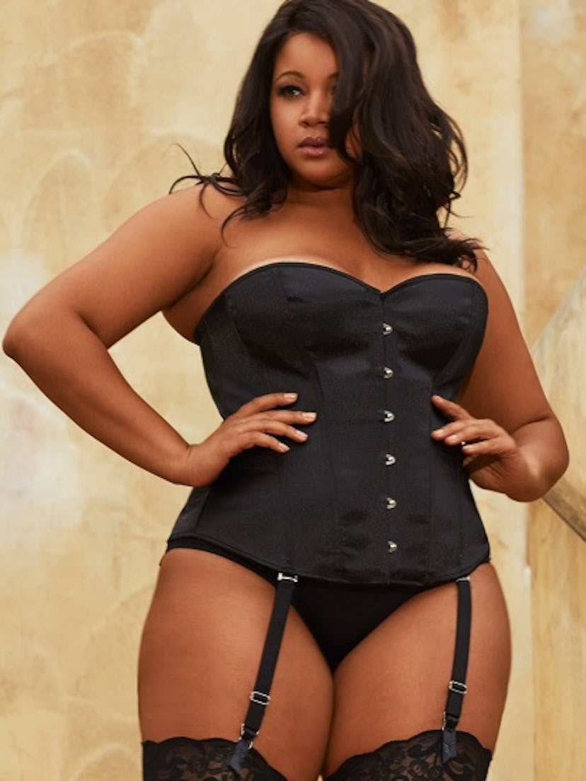 A plus size model posing in a black satin corset