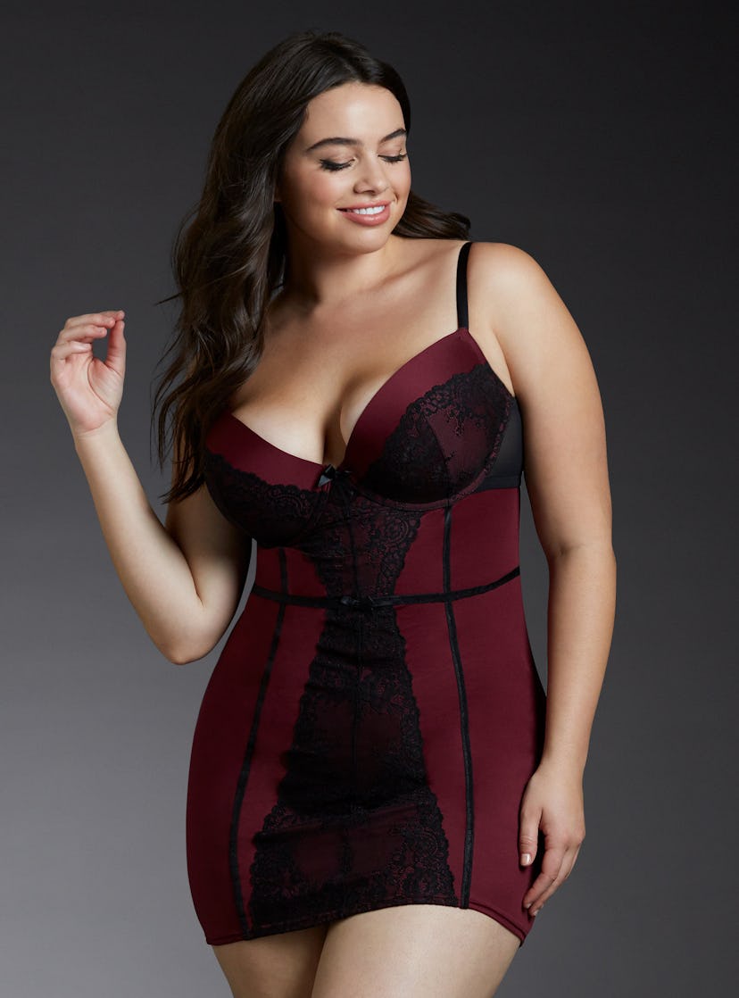A plus size model posing in a red and black lace and fishnet chemise