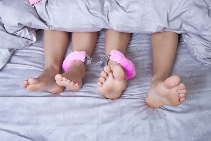 The feet of two people using pink fur cuff sex toys 