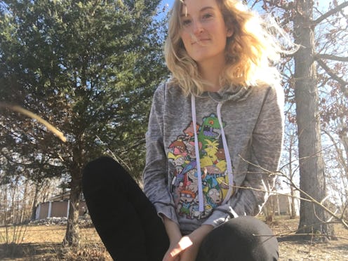 A young blonde woman wearing a graphic grey hoodie and black leggings sitting in woods
