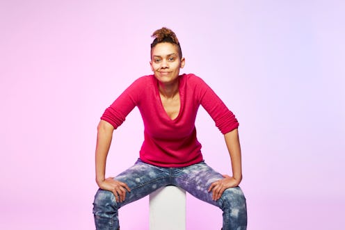 A woman in a red t-shirt and jeans sitting while leaning on her knees