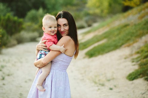 A young mother wearing a lavender dress holding her toddler dressed in a pink shirt and plaid shorts