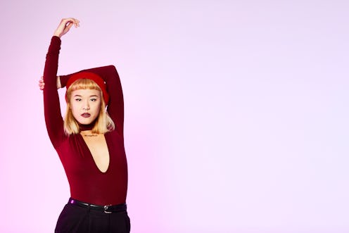 A blonde woman in a burgundy top and black pants stretching her right arm while posing for a photo