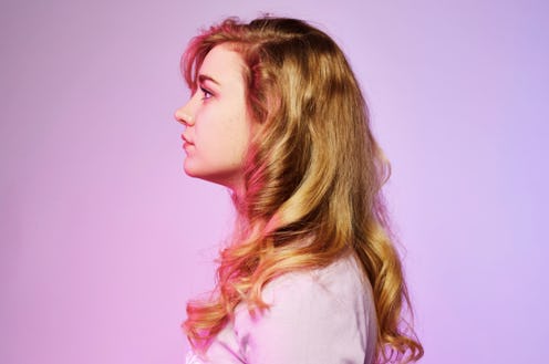 A side portrait of a woman standing in front of a pink/purple background