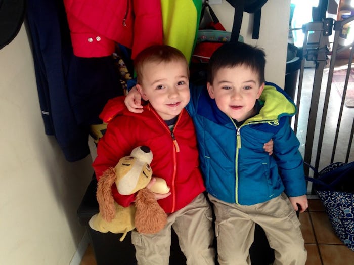 Two little boys sitting down, one is in a red coat and holding a dog toy, while the other is in a bl...